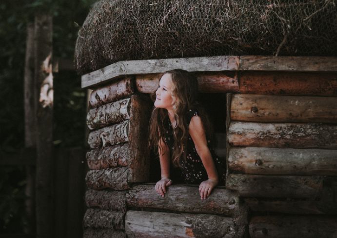 The girl is looking out of the window of a wooden cottage