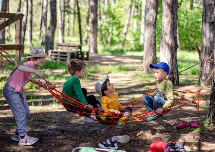 Children are swinging on a hammock in the forest