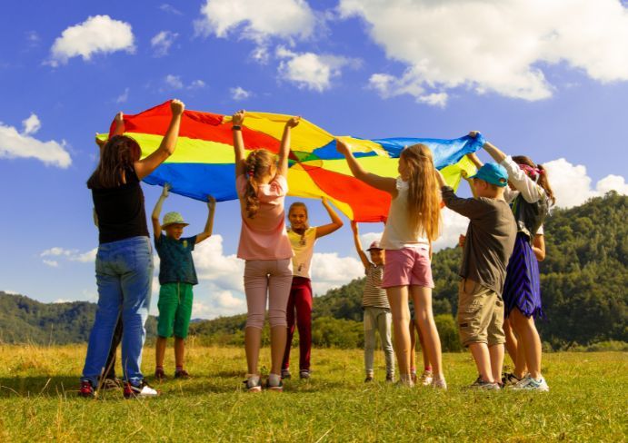 children stand in a circle in a clearing and hold a colorful canvas